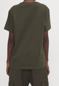 Camiseta de algodón verde oliva con mangas cortas, ajuste relajado y escote redondo. Textura suave; las costuras están doblemente cosidas para mayor durabilidad.