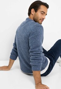 Maglione a maglia blu chiaro con colletto e polsini a costine, materiale testurizzato, indossato sopra una camicia bianca, seduto su uno sfondo semplice.