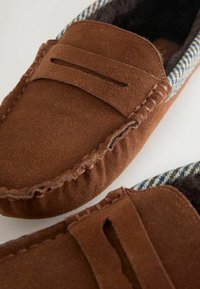 Ruskeat mokkanahkaiset mokkasiinit, joissa on ruudullinen koriste kauluksessa, tikatut yksityiskohdat ja pehmeä sisävuori mukavuutta varten.