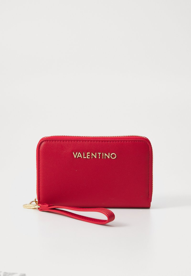 Raudona odinė piniginė su auksine užtrauktuku, kuri priekyje turi išliejamą prekės ženklą "VALENTINO". Į komplektą įeina riešo dirželis nešimui.