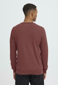 Burgundy színű pulóver hosszú ujjal, bordás mandzsettákkal és aljjal. Puha tapintású, kerek nyakkivágású, minimalista dizájnnal. Hátsó nézet látható.