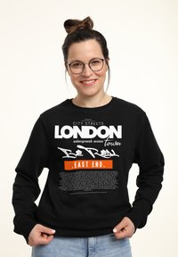 Svart sweatshirt med djärv vit och orange text som visar "London" och "East End", med en lös passform och ribbade mudd.
