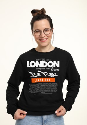 Czarny sweatshirt z wyraźnym białym i pomarańczowym napisem, zawierającym słowa "Londyn" i "East End", w luźnym kroju oraz z ściągaczami przy rękawach.