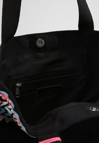 Bolsa de tela negra con un ribete colorido y estampado, un bolsillo interior con cremallera, un compartimento principal con cierre de presión y asas de transporte negras y resistentes.