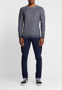 Marineblauwe gebreide trui met een gestructureerde afwerking, gecombineerd met marineblauwe cargobroek en zwart-witte sneakers met veters en een lage zool.