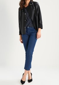 Svart skinnjacka med en textured design, ihop med en mönstrad topp, blå jeans och svarta högklackade skor.