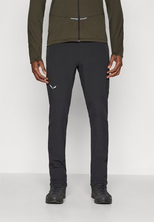 Schwarze Outdoor-Hosen mit schmaler Passform und elastischem Bund. Sie verfügen über verstärkte Knieflecken und ein weißes Logo-Detail am Oberschenkel.
