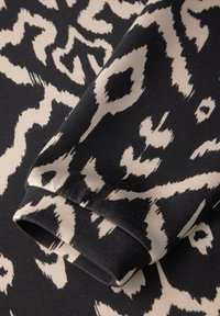 Tessuto nero con un motivo astratto beige, dal tocco liscio. Il design include forme e linee irregolari.