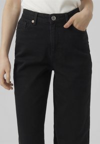Jeans neri a vita alta in denim, con chiusura anteriore a bottone, tasche laterali e un design dritto. Texture liscia.