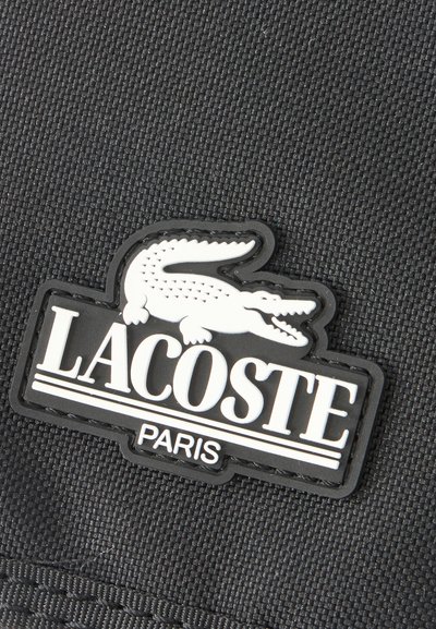 Черна текстурирана тъкан с черно-бяло лого Lacoste Paris, показващо крокодил над името на марката.