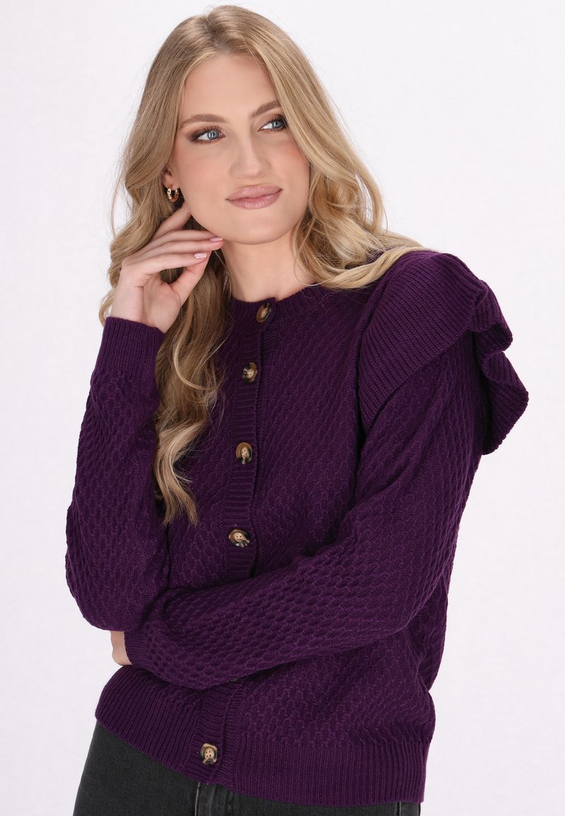 Purple knitted cardigan with a textured pattern, ruffled shoulders, and five brown buttons along the front. Fitted design with long sleeves.