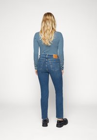 Modré džíny s rovnými nohavicemi a vysokým pasem se dvěma zadními kapsami, doplněné dlouhým rukávem a námořnicky modro-bílým pruhovaným topem.