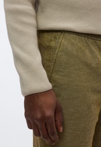 Μανίκι μπεζ πλεκτού με ραβδώσει ς συνδυασμένο με ελιά πράσινο παντελόνι που διαθέτει διακριτικό υφασμάτινο μοτίβο και μικρό κεντημένο λογότυπο κοντά στη μέση.