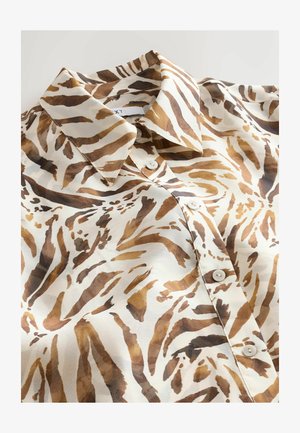 Bluzka z kołnierzykiem w jasnym kremowym kolorze, z odważnym brązowym i beżowym zwierzęcym wzorem, o gładkiej fakturze i białych guziczkach zapinanych z przodu.