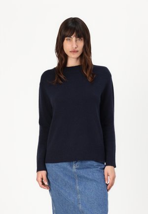 Navy knitted sweater with a crew neck, dropped shoulders, and ribbed hem. Paired with a denim skirt, showcasing a casual, layered look.