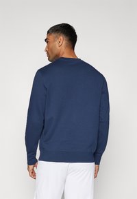 Navyblå sweatshirt med lange ærmer, rund hals og en glat tekstur; har ribbede manchetter og kant, minimalistisk design.