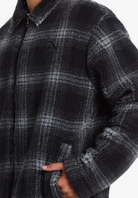 Black and gray plaid fleece jacket with a zip front, collar, long sleeves, and two side pockets. Soft texture with a checkered pattern.