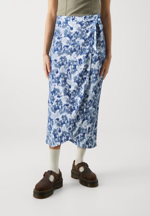 Falda midi floral azul y blanca combinada con una blusa beige, calcetines blancos y zapatos Mary Jane gruesos de color marrón oscuro sobre un fondo liso.