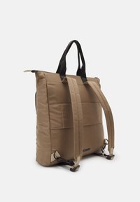 Tan nylon draagtas met zwarte handvatten en verstelbare schouderbanden. Voorzien van een geruit ontwerp en gespaccenten. Minimalistische esthetiek.