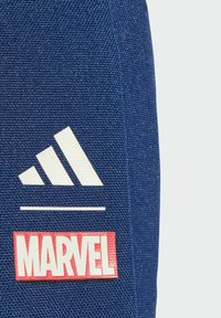 Tmavomodrá tkanina s bielym logom Adidas so tromi diagonálnymi pruhmi nad červeným obdĺžnikovým logom Marvel. Detail textúry povrchu.