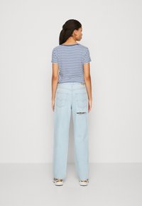 Stribet blå og hvid cropped t-shirt parret med lyseblå vide jeans, der har et hul på højre lår og baglomme.