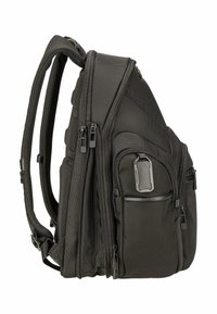 Sac à dos noir à plusieurs compartiments avec des bretelles rembourrées, plusieurs poches zippées et une petite étiquette de bagage noire attachée.