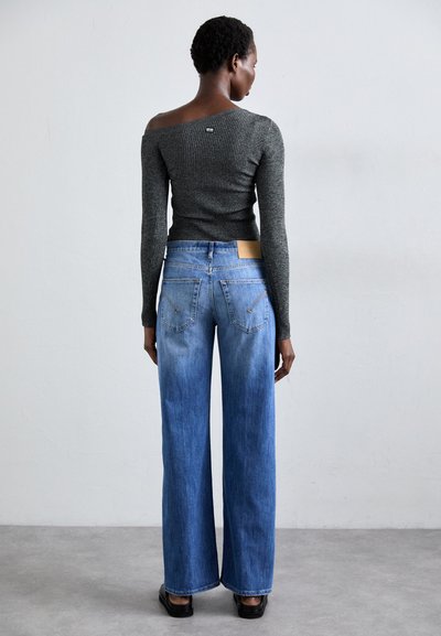 Gray ribbed long-sleeve top paired with light-blue wide-leg jeans. Visible back pockets with zippers and a tan leather label on the waistband.