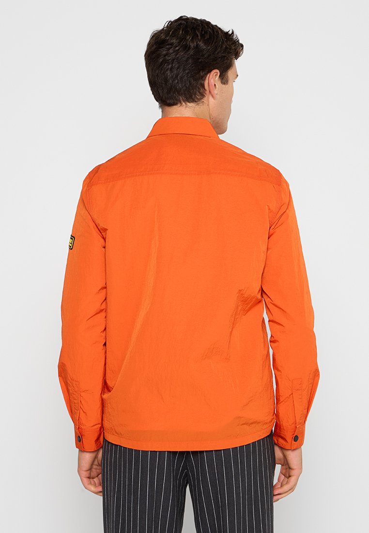 Oranges Hemd mit Button-Down-Kragen, langen Ärmeln und einem kleinen Logo-Patch auf der linken Schulter. Aus leichtem Stoff gefertigt.