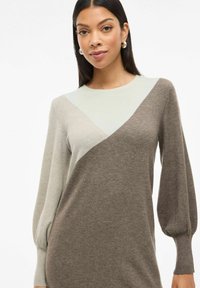 Abito lavorato a maglia con design a blocchi di colore in tonalità verde chiaro e marrone, maniche lunghe a sbuffo e silhouette rilassata. Texture liscia.