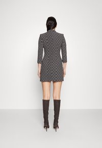 Frau, die mit dem Rücken steht, trägt ein schwarz-weiß gemustertes Kleid und kniehoge, dunkelbraune, samtige Stiefel mit Absätzen.