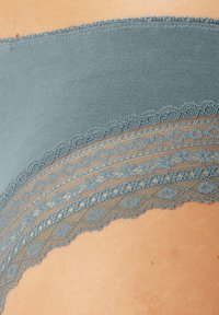 Grijze stoffen tas met delicate kantafwerking met geometrische patronen en golvende randen. Zachte textuur; subtiele, elegante designelementen.