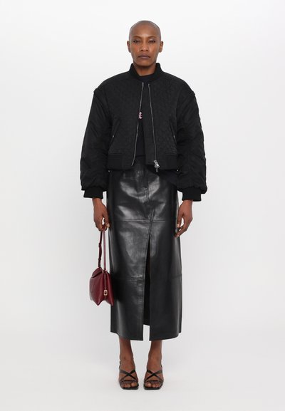 Giacca bomber nera trapuntata con polsi a costine, abbinata a una gonna di pelle nera con uno spacco frontale. Accessoriata con una borsa bordeaux.