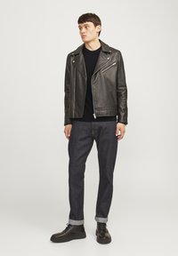 Svart läderbikerjacka med asymmetriska dragkedjor, kombinerad med en svart tröja, mörka jeans och svarta snörboots.