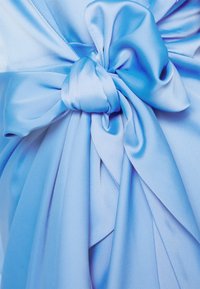 Tissu satiné bleu clair doux noué en un grand nœud lisse avec des plis fluides et une texture brillante et soyeuse.
