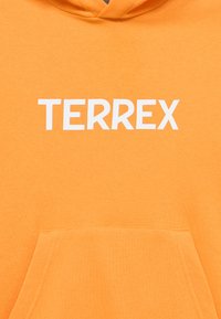 Πορτοκαλί φούτερ με κουκούλα και τσέπη καγκουρό, φτιαγμένο από μαλακό ύφασμα, με την λέξη "TERREX" σε έντονα λευκά γράμματα στο στήθος.