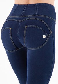 Leggings a vita alta blu navy con una texture liscia, caratterizzati da cuciture gialle e due tasche posteriori curve con un piccolo accento di logo.