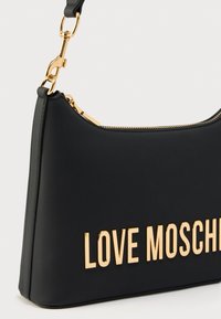 Μαύρη συνθετική τσάντα χειρός με λεία υφή, καμπυλωτό σχήμα, χρυσά μεταλλικά στοιχεία και το λογότυπο "LOVE MOSCHINO" σε εμφανές χρυσό.