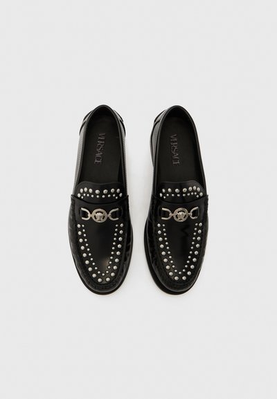 Mocasini negri din piele, decorați cu ținte argintii pe partea superioară și un accent metalic circular, cu un finisaj neted și lucios și tălpici marcate cu brand.