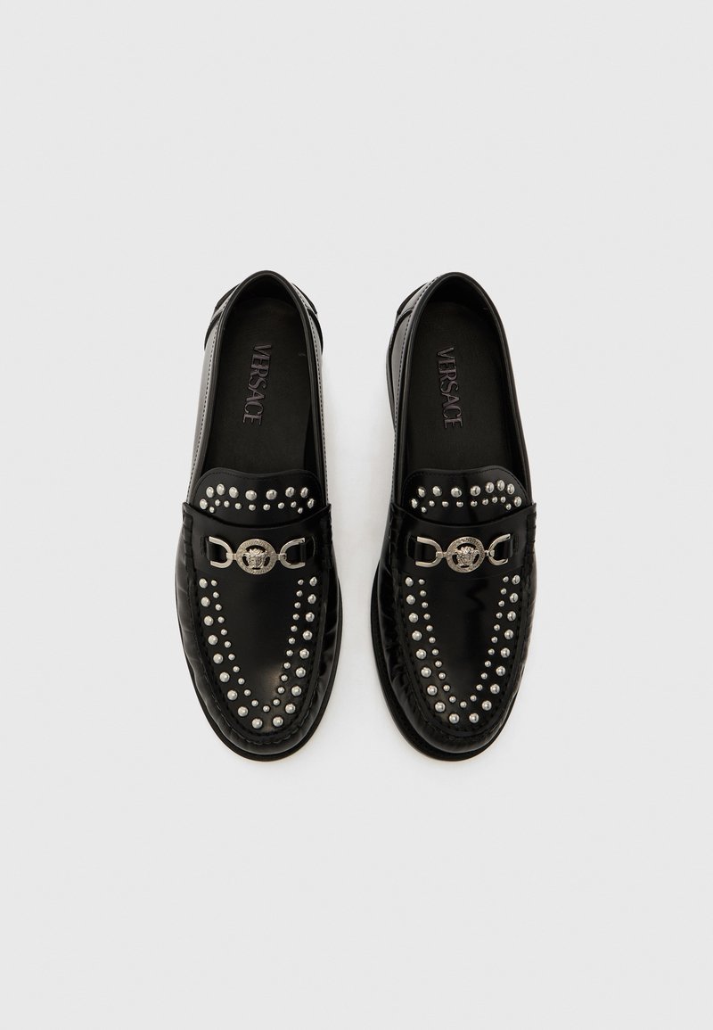Mocassini in pelle nera con borchie argento sulla tomaia e un elemento circolare metallico, con finitura liscia e lucida e plantari con marchio.