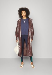 Skinande bordeaux lång kappa, marinblå sweatshirt, svarta leggings med gröna detaljer, vita knutna klackar och gräddfärgad axelväska.