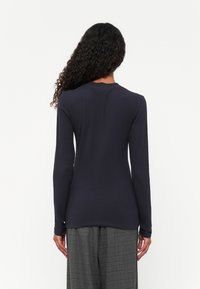 Mørkeblå ribbet langermet topp med rund hals, tettsittende fasong og sideslittsdetaljer, kombinert med grå rutete vide bukser.