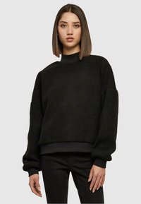Zwarte fleece sweatshirt met hoge hals, drop shoulders en geribbelde mouwen. Zachte textuur, cropped lengte en eenvoudig ontwerp. Draag het over zwarte broek.