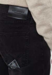 Tascone di jeans in denim nero con etichetta triangolare Roy Roger's e toppa in pelle del marchio, indossati con un maglione di lana beige.