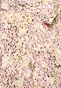 Tissu beige clair avec un motif irrégulier de léopard en rose, blanc et noir, et un détail de ceinture nouée sur le côté supérieur droit.