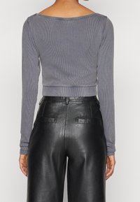 Grå ribbad långärmad crop top tillsammans med svarta läderbyxor med hög midja som har en slät yta och två bakfickor.