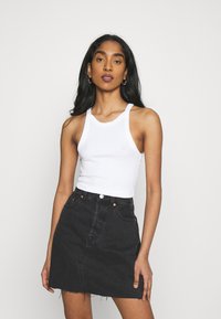 Top de alças branco com textura canelada, combinado com uma saia de ganga preta de cintura alta, apresentando uma bainha desfiada e detalhes em botão de cobre.