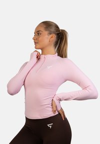 Jasnoróżowa, długorękawowa bluzka sportowa z suwakiem na pół, z delikatną fakturą i małym białym logo na piersi.