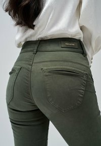 Olivově zelené přiléhavé džíny s vysokým pasem, dvojnásobnými zadními kapsami a kovovým logem na pásku. Hladká bavlněná tkanina.