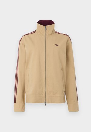 Veste beige avec col montant, fermeture éclair et deux poches latérales. Présente des accents rayés bordeaux sur les manches et un petit logo sur la poitrine.
