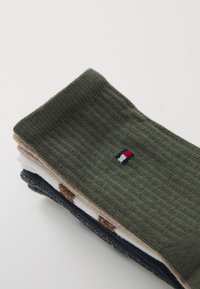 Lot de quatre chaussettes : chaussette côtelée vert foncé avec logo, olive, beige et marine avec un motif à pois, en tissu tricoté texturé.
